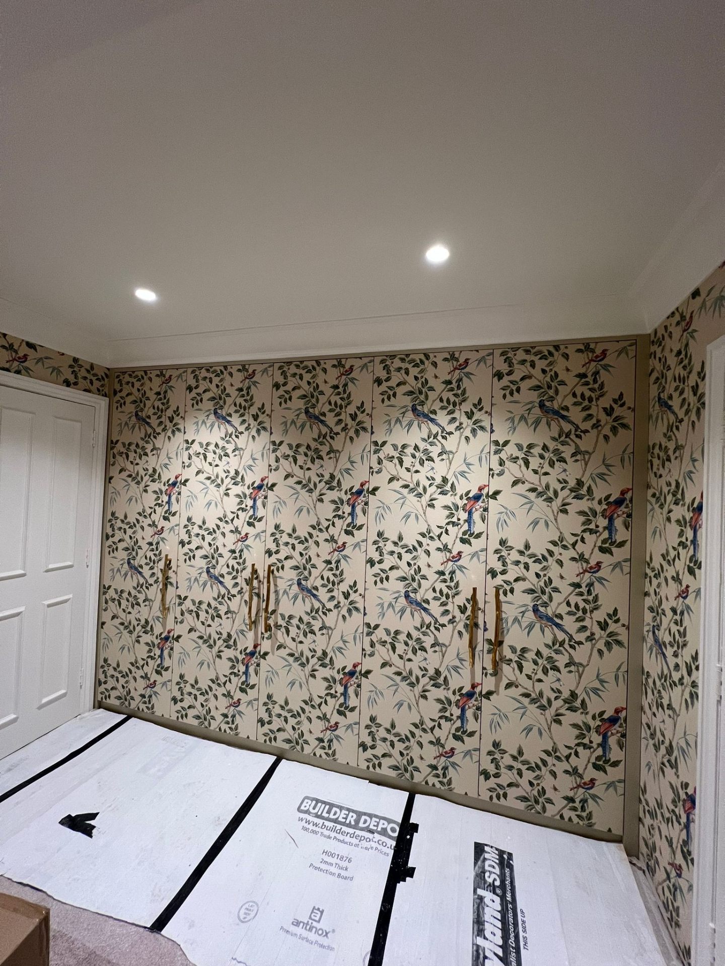 Bespoke fitted wardrobe with hand-applied bird-and-foliage wallpaper door panels and brass twig handles, bedroom refurbishment