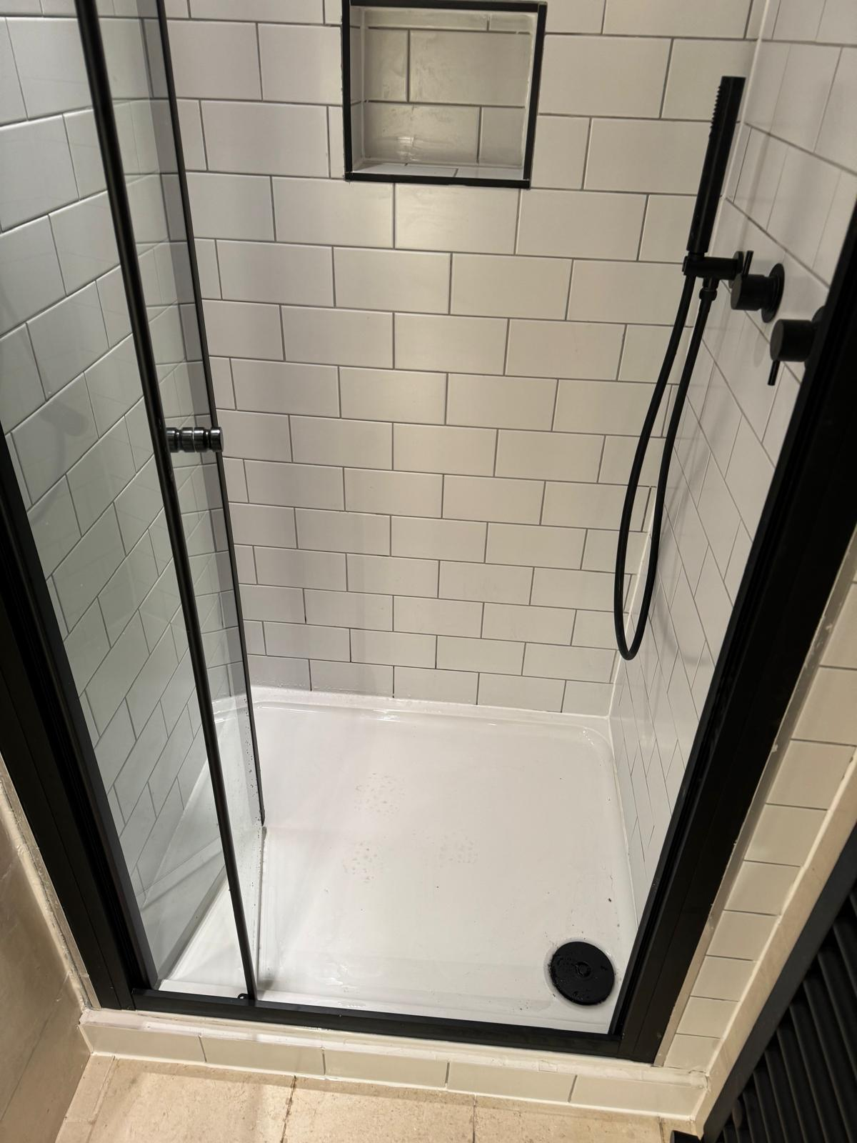 Walk-in shower enclosure with white metro tiles, matte-black fittings and tiled niche shelf
