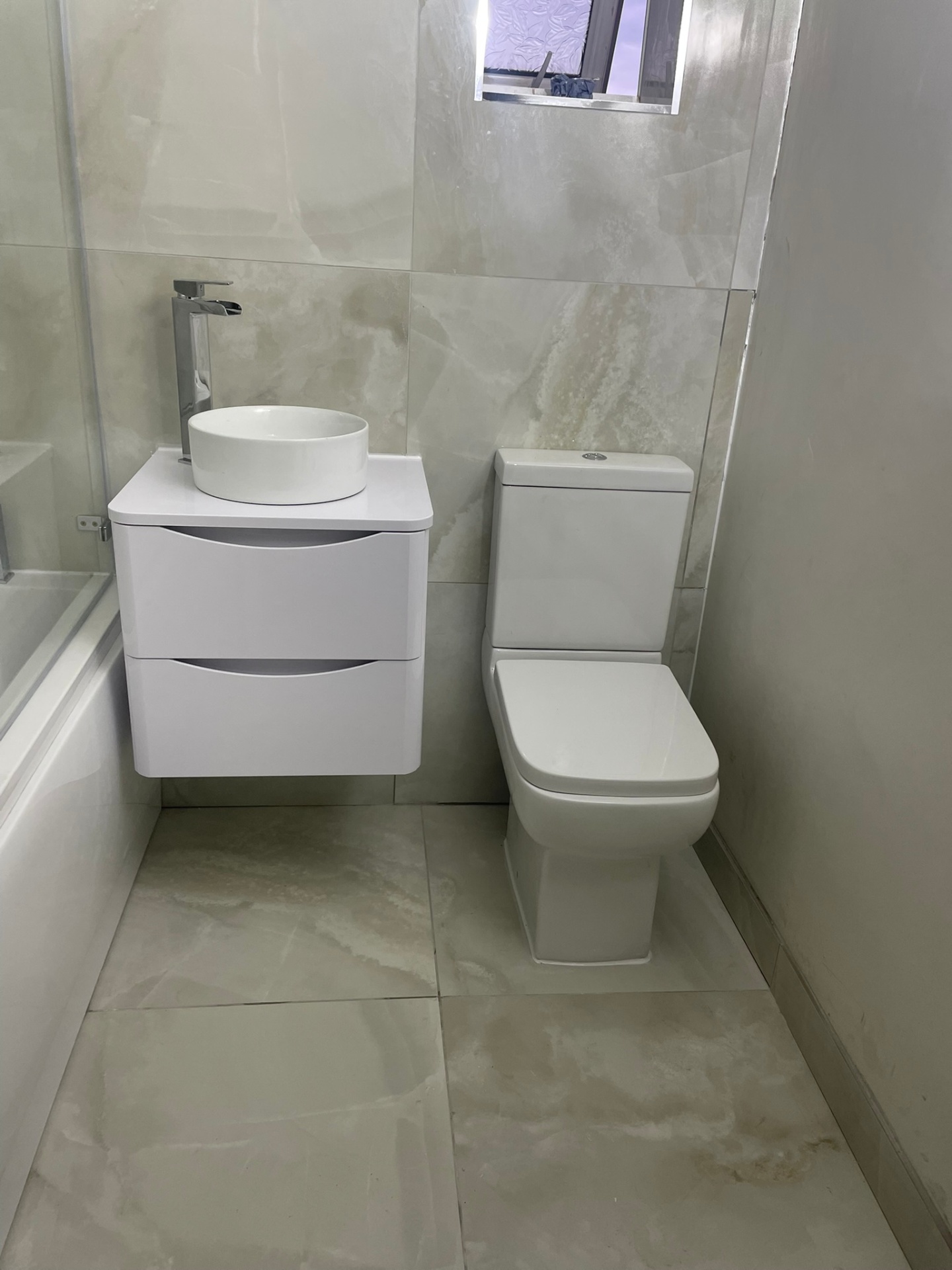 Bathroom vanity unit with countertop vessel basin and chrome tap on marble-effect wall tiles, installed in West London