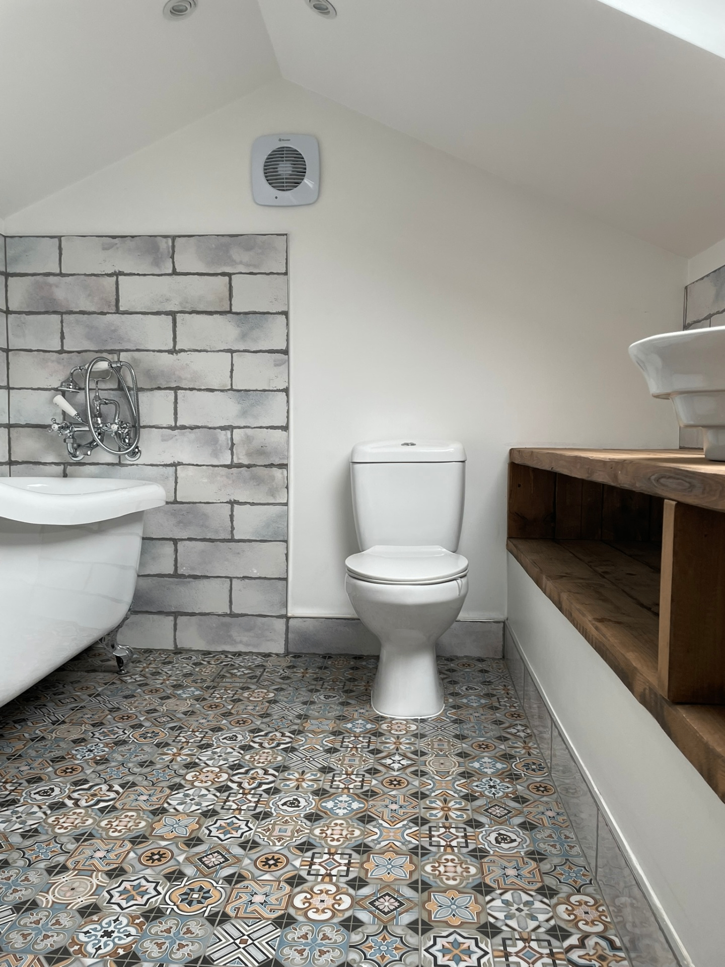 Loft bathroom with roll-top bath, patterned floor tiles and reclaimed timber shelving — Ash Villa install, West London