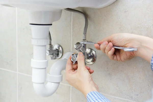Plumber using an adjustable wrench to tighten a chrome basin tap connection with braided flexi hose and white push-fit waste pipe below — Ash Villa Gas Safe plumbing in West London