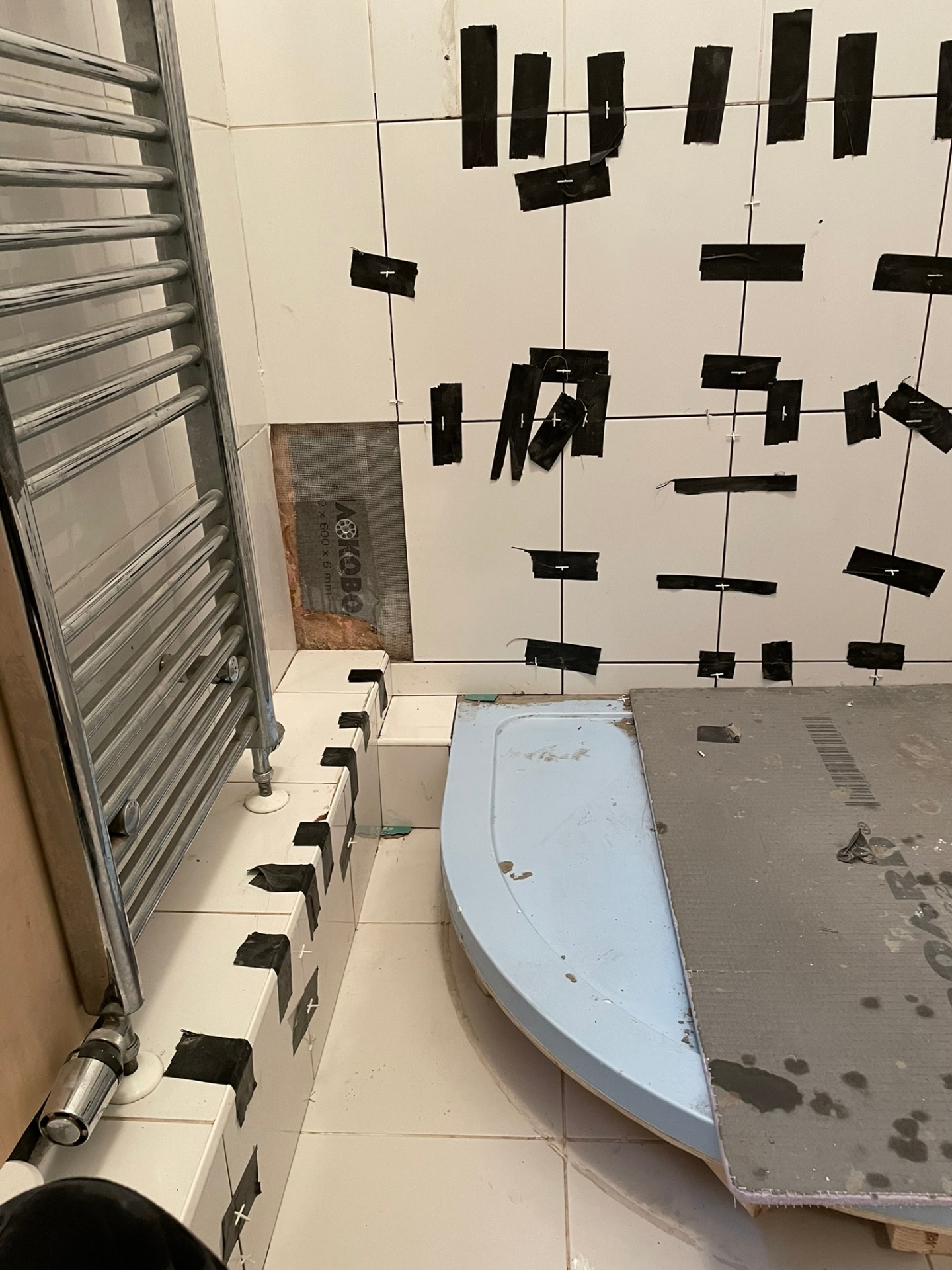 Bathroom tiling in progress with white square wall tiles, levelling clips and quadrant shower tray being fitted