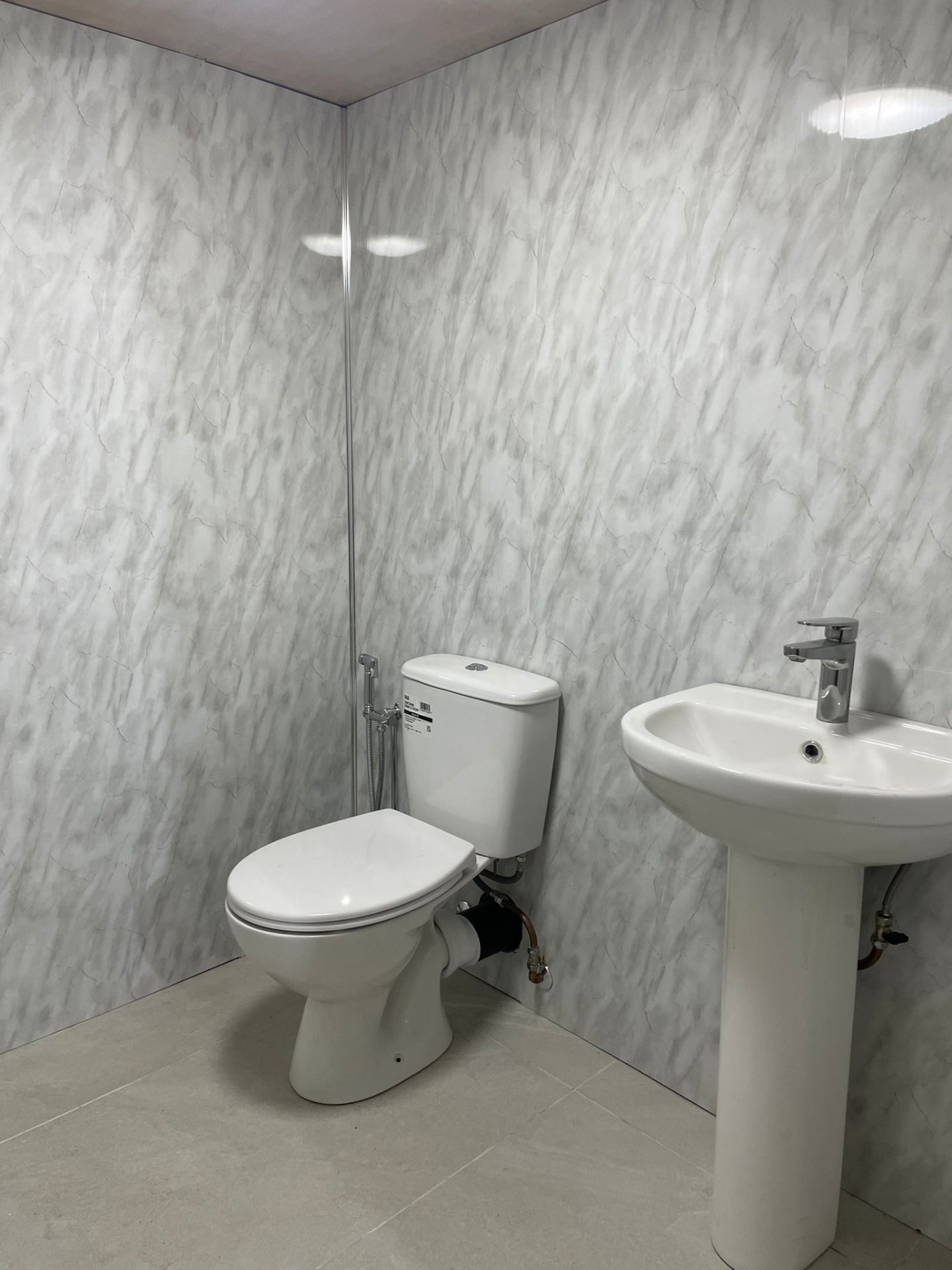 Cloakroom fitted with marble-effect PVC wall panels, close-coupled WC and pedestal basin, West London installation