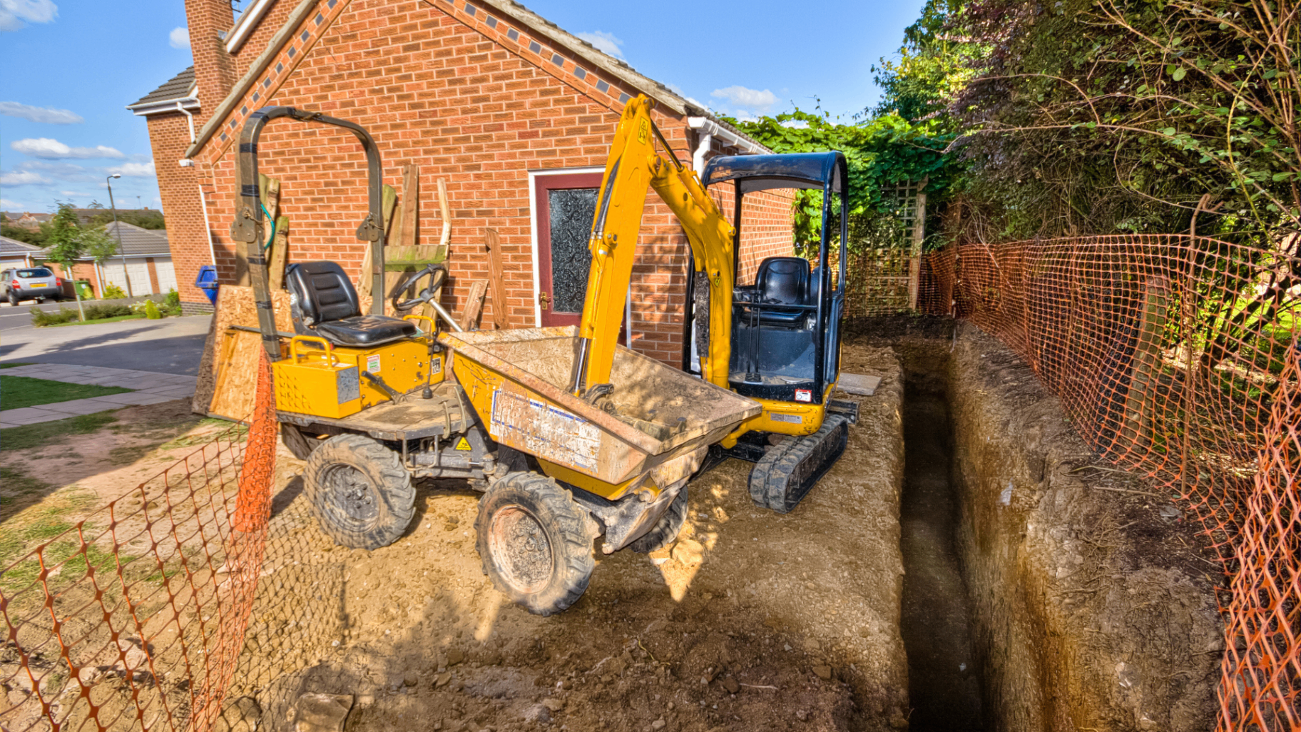 Mini-excavator digging foundation trenches beside a brick house — Ash Villa extension groundworks in West London