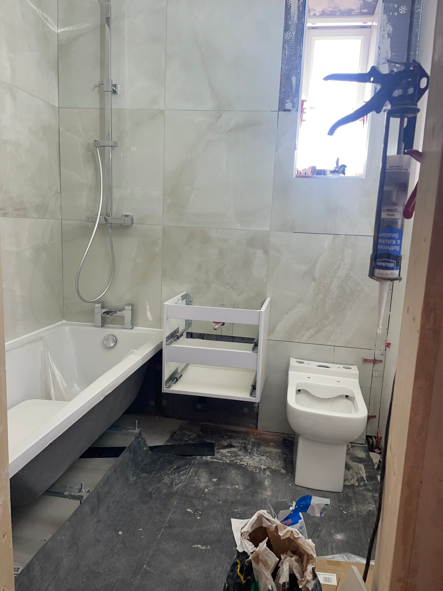Bathroom installation in progress showing a new white bath, floating vanity frame and wall-hung toilet on marble-effect tiles