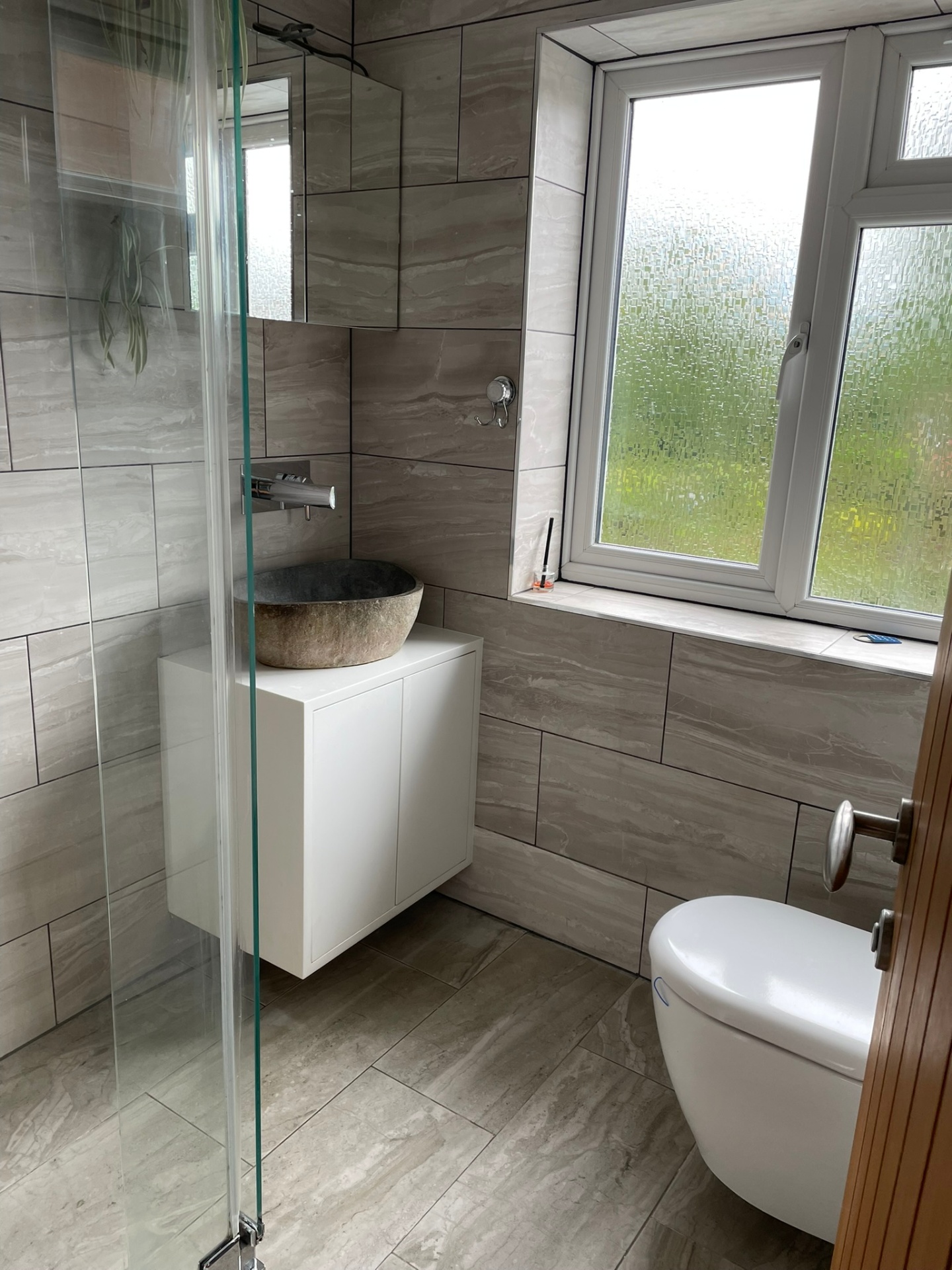 Modern bathroom installation with stone vessel basin, wall-mounted tap and walk-in shower on marble-effect tiles by Ash Villa, Acton
